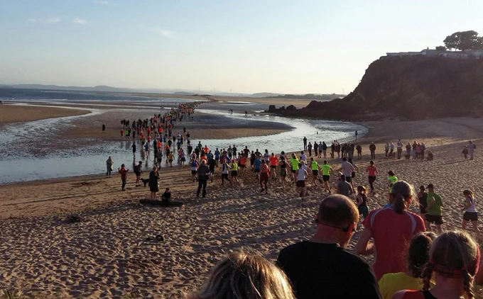 Hundreds of runners going out across the sand at low tide