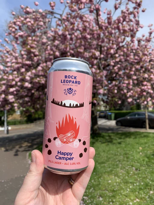 Pink can with a red campfire in the middle. Rock Leopard and ‘Happy Camper in blue type and the style, abv in red type.