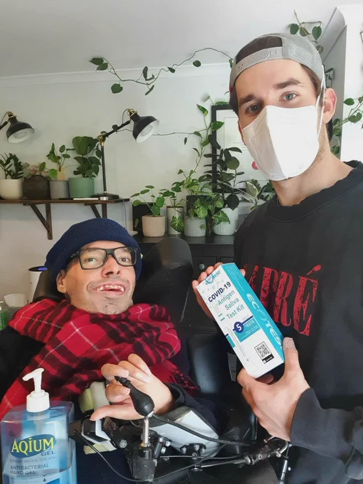 George Taleporos and man with mask, sanitiser and rapid antigen tests. There are plants in the background and George is wearing a beanie and scarf