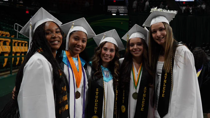 Five graduates in white gowns pose for a picture during graduation ceremony