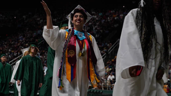 Graduate waving to the crowd during graduation ceremony.