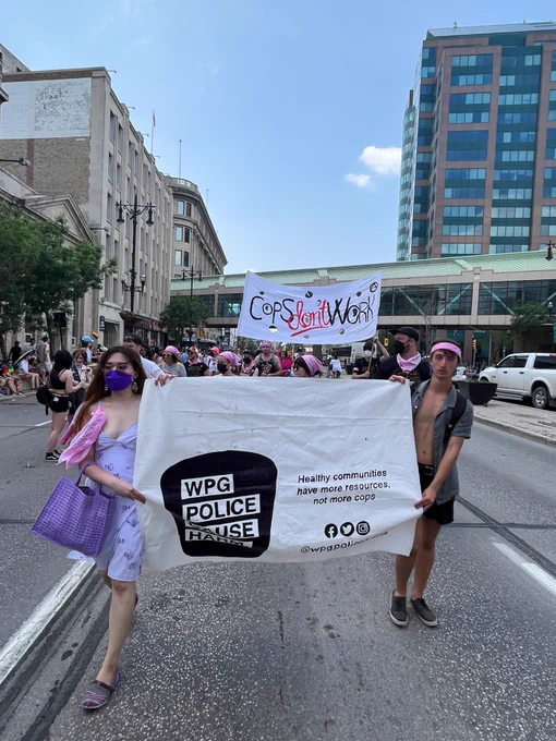 Two people hold a WPCH banner while walking that reads "healthy communities have more resources not more cops" and behind it is a banner that says "Cops don't work"