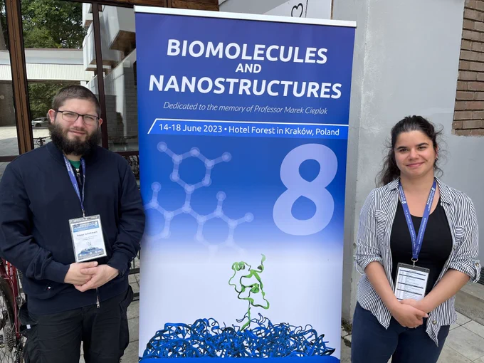 A banner of the scientific conference and two young scientists standing on each side.