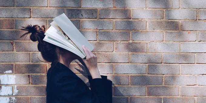 Eine junge Frau hält ein aufgeschlagenes Buch vor ihr Gesicht