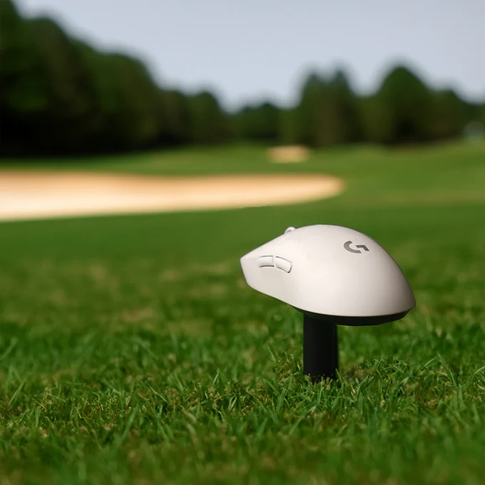A Logitech G PRO X Superlight resting on a golf tee. A golf course is in the background with a bunker and trees that are visible.