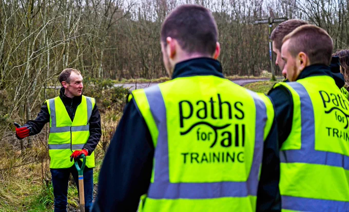 three men in high visibility vests gather on a path to talk