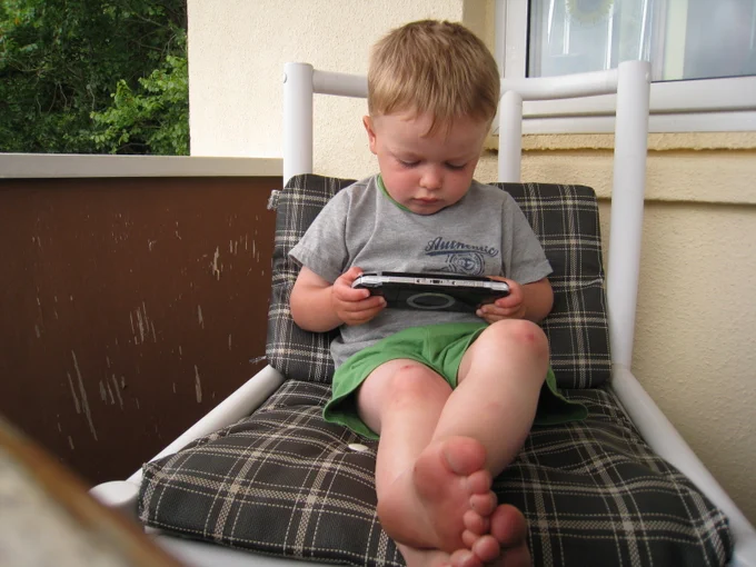 Small boy sits on lounger playing PSP.