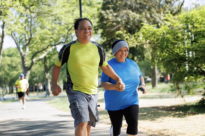 Two runners holding hands running on a path in a park.