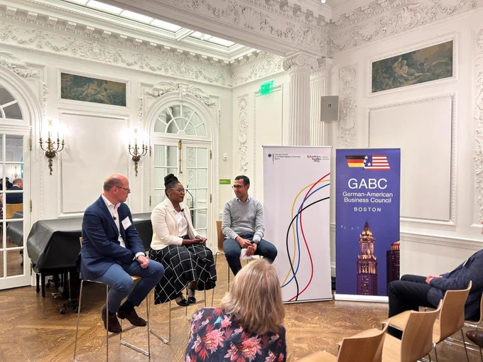 A picture of the speakers and moderator sitting on high chairs in front of an audience. From left to right is Sebastian Guth, Fiona Mack and Dr. Mridul Agrawal