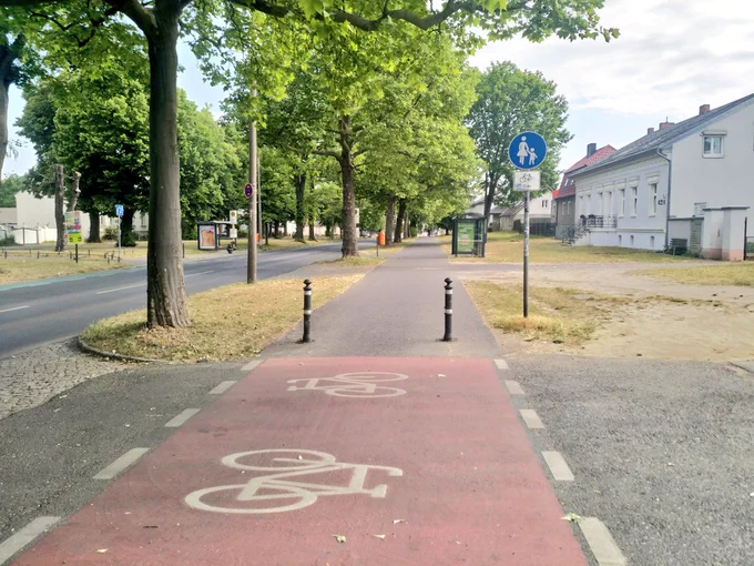 Kreuzung ist wie ein Radweg in Rot markiert. Der Weg dahinter hat eine Beschilderung Fußweg - Fahrrad frei