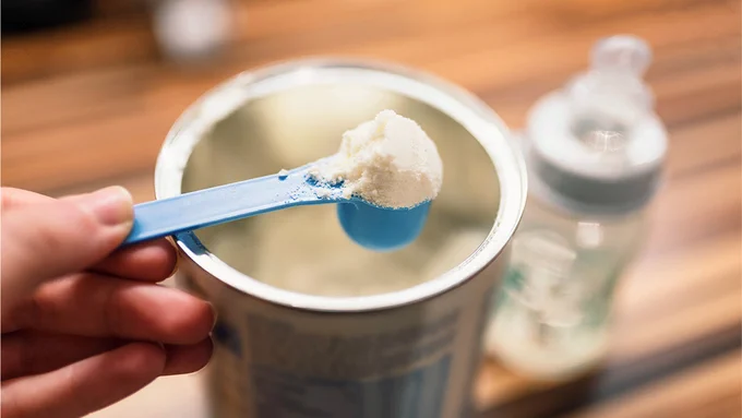 Hand holding a teaspoon of toddler milk.