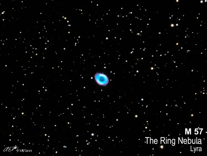A swatch of black space punctuated with stars and galaxies. At the center is the oval Ring Nebula in electric blue ringed with magenta. At the bottom left is the photographer's signature AE Perkick and the bottom right are the words M 57 | The Ring Nebula | Lyra. 