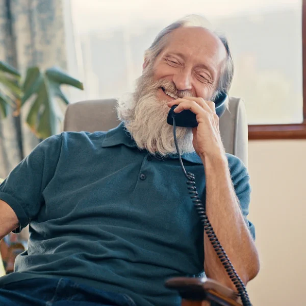 An older-aged man on a landline telephone is enjoying a casual conversation in his home.
