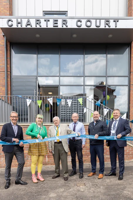 A group of people standing in front of the former office block cutting a blue ribbon to open the new affordable homes. 