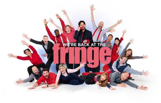 A group of 20 performers doing jazz hands arranged in a circle around a sign saying "We're back at the Fringe"

