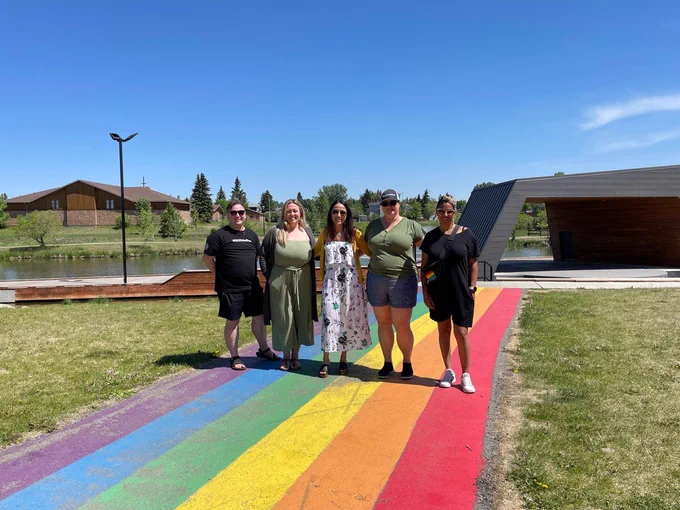 Five team members stand arm in arm on a rainbow sidewalk