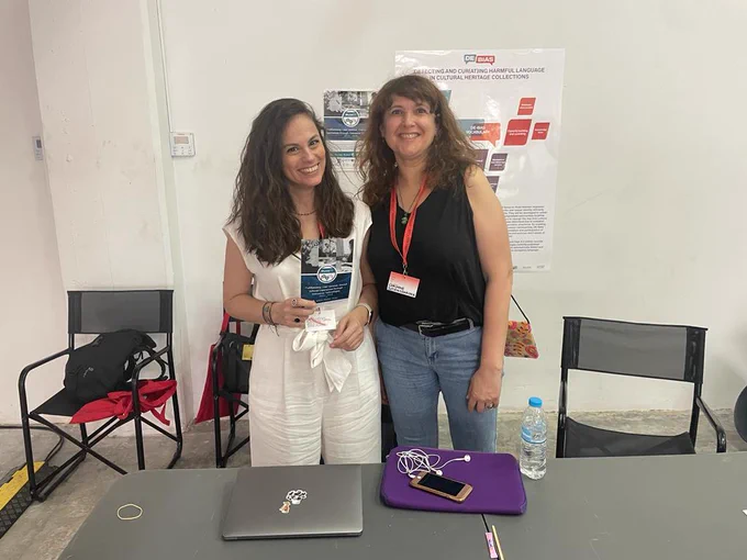 Picture of Georgia Georgiou and Corinne Szteinsznaider.
They are smiling and standing beside each other, behind the MuseIT desk at the forum. In the background, there is the MuseIT Poster.