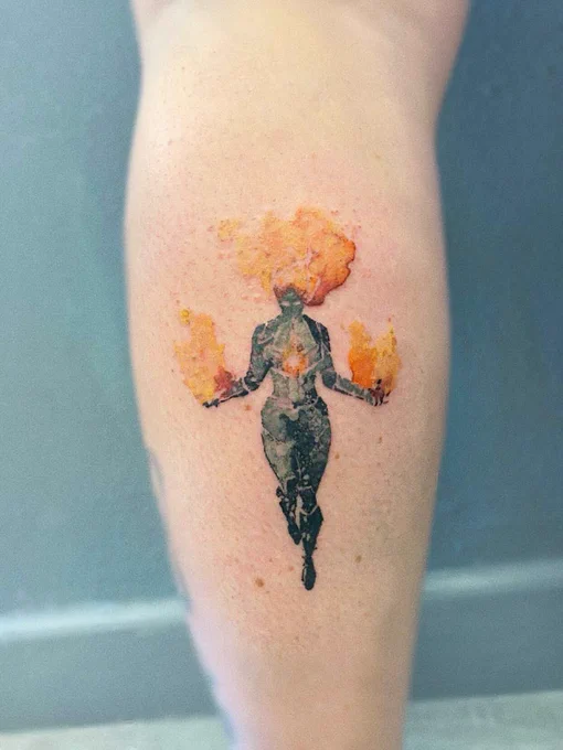 Picture of the back of my calf, showing a watercolor-style tattoo of Captain Marvel. Her body is in black and white but her arms, head, and chest glow with red-orange flame.
