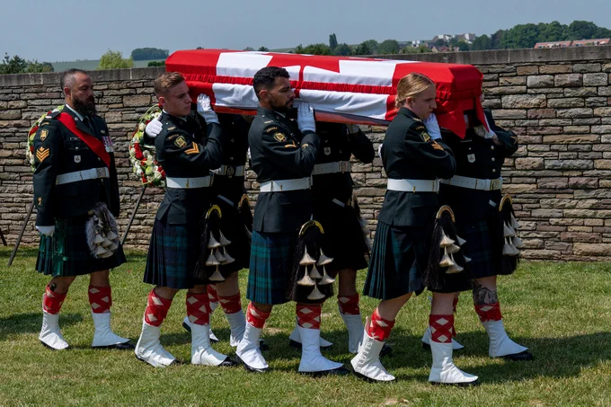 Six Canadian Armed Forces soldiers carry a casket draped in a red and white Canadian flag in Loos British Cemetery in Loos-en-Gobelle, France.