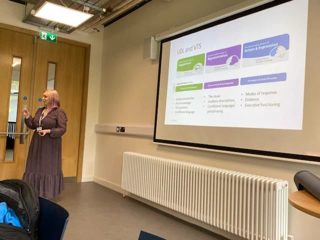 Margaret speaking with delegates standing to the side of her presentation slides