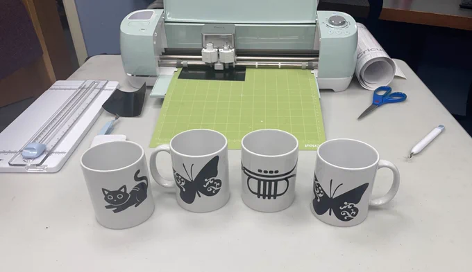 4 mugs with designs in front of a Cricut machine