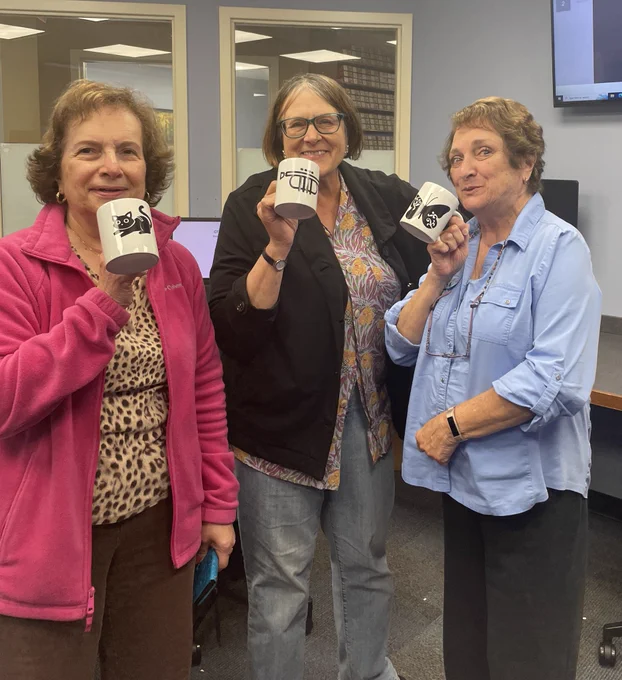 3 women holding up mugs that they made, one pretending to drink from it.