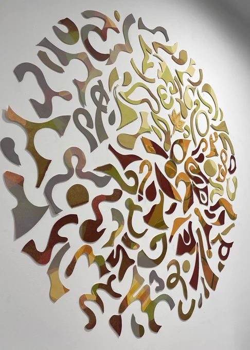 An abstract circular artwork. The circular piece is created from smaller abstract shapes in warm green, red, orange and yellow hues.