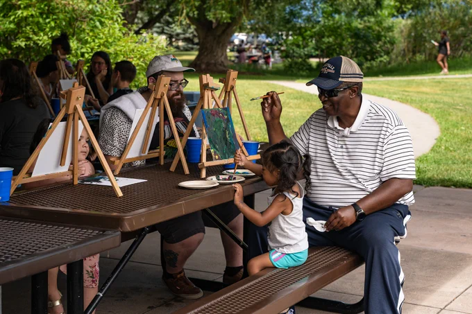 A group of adults and children smile while painting on canvases.