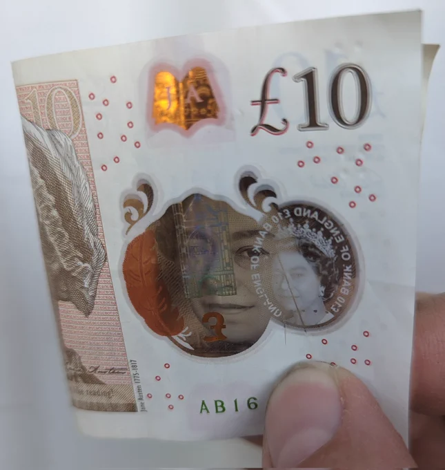 A ten pound note folded so that the Queen is smiling through the security window