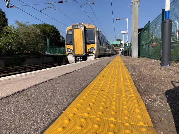 Yellow tactile paving on a train platform with a train pulling in in the background