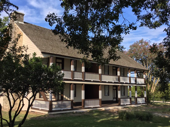 Photo of the Lewis-Wagner House, a two-story light beige building with dark brown and white trim, at Winedale.