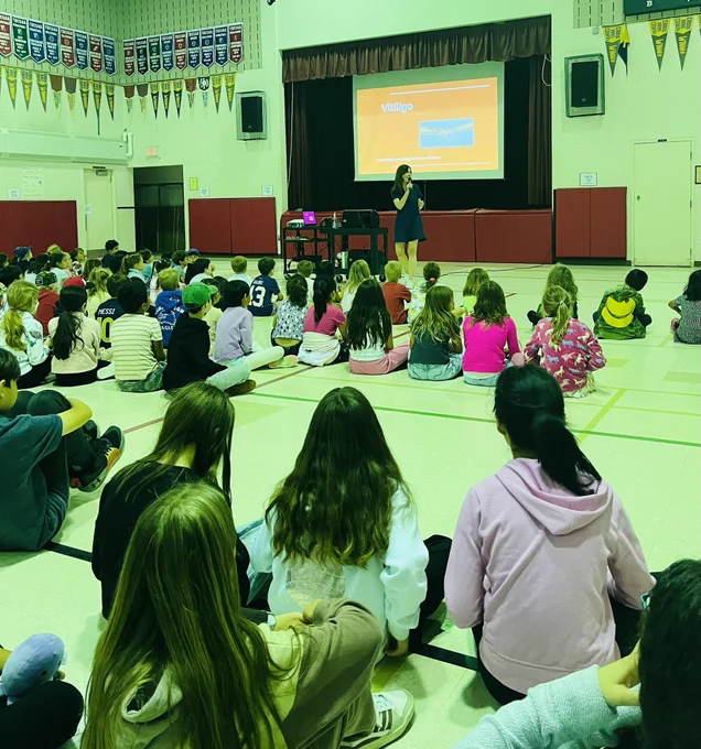 Students sitting on the floor of the gymnasium watching a presentation.