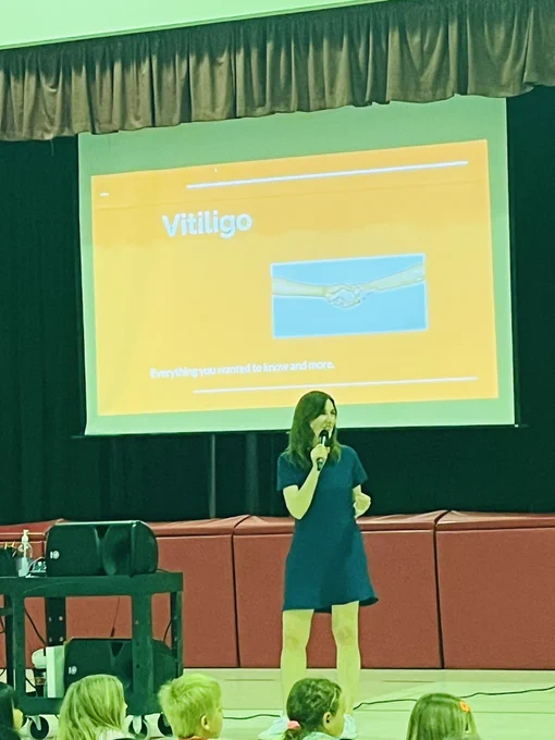Ms George Hughes standing in front of gymnasium stage speaking into a micro phone.