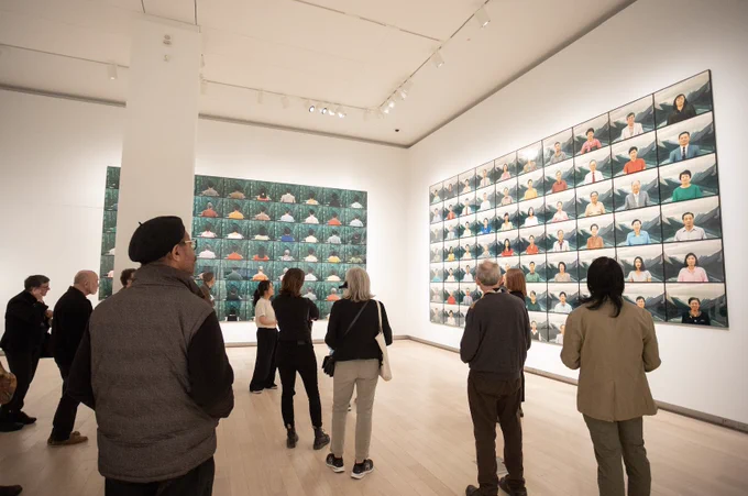 A photograph of a group of people at the Image Arts Centre Gallery viewing the Scotiabank Photography Award: Jin-me Yoon. The walls are filled with portraits that most guests look up to view. 
