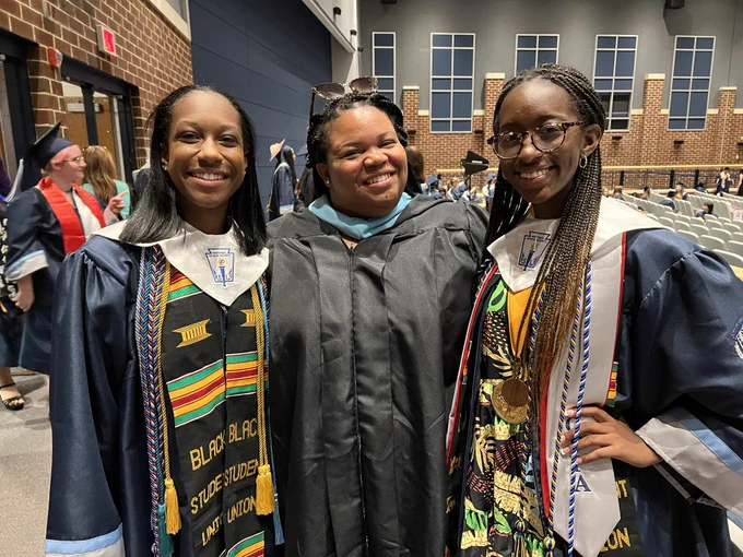 Two graduates and one teacher dressed in gowns stop for a picture together before the ceremony.