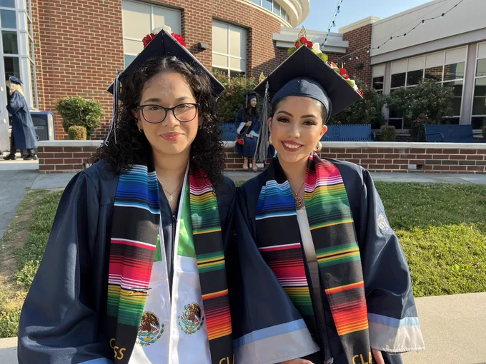 Two graduates pictured in gowns and caps pose before the ceremony.