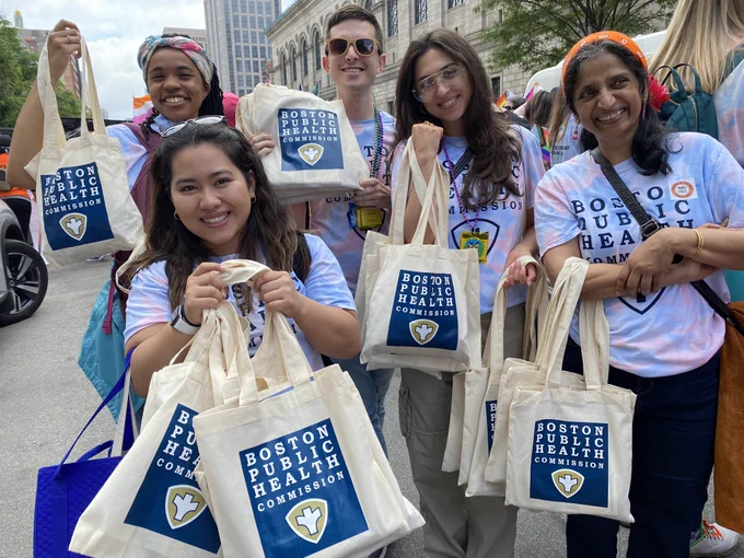 A group of BPHC staff holding bags full of health and wellness supplies for residents.