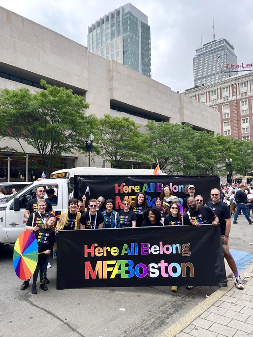 Group of people stands with a sign that says "Here All Belong, MFA Boston"