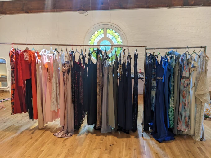 Prom dresses on a rail, from red on the left through pink and black to blues and greens on the right.