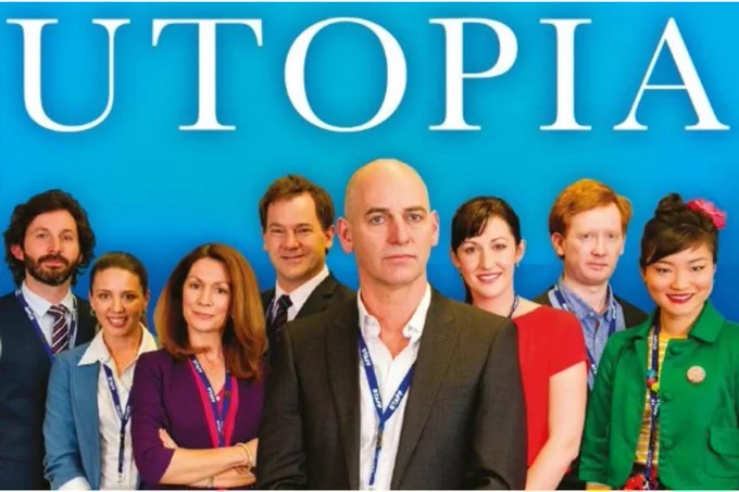 The cast of the ABC television series 'Utopia', staring Rob Sitch, Cella Pacquota, Dave Lawson, Emma-Louise Wilson, 'Lehmo', and Kitty Flanagan. Image also features Luke McGregor and Michelle Davidson. All are in business attire with workplace lanyards. All are smiling except main character Tony (Rob Sitch), who looks thoroughly frustrated.