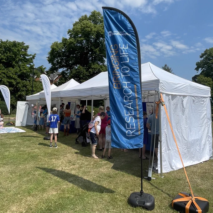 A gazebo at an event with a flag outside. The flag has the university of southampton logo and the words 
‘Bringing research to life’ on it.