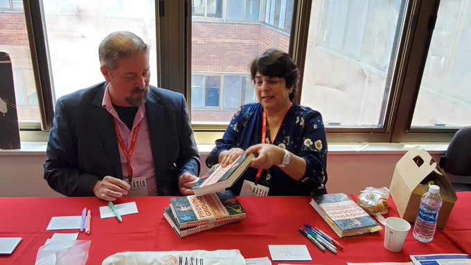 Photo of Jothan Frakes sitting with Author Kathy Kleiman at a desk where she is about to sign a copy of her book for him