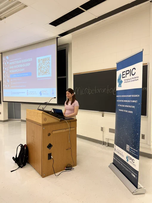 Maxine Ty standing at a podium with an EPIC banner and blackboard in the background.