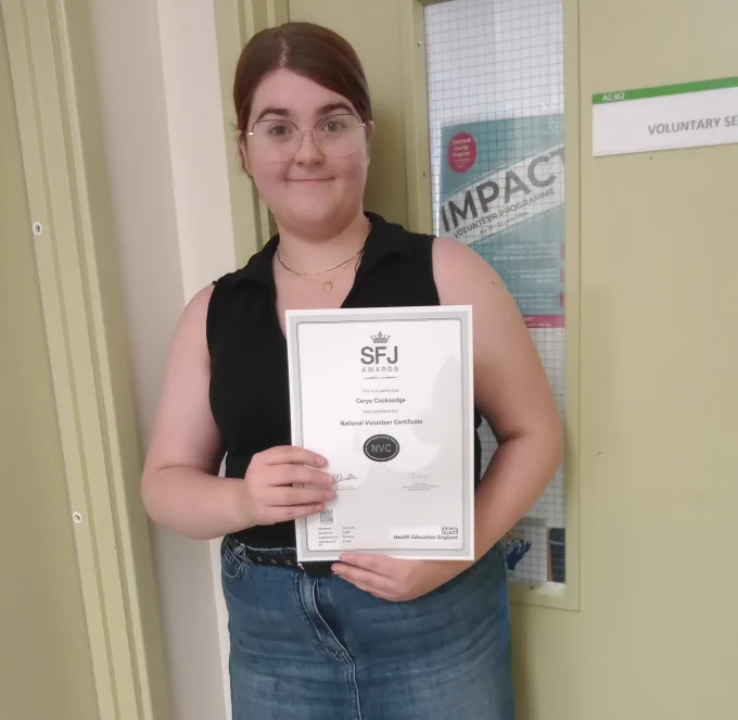 Cerys is standing outside the voluntary services room with her National Volunteer Certificate