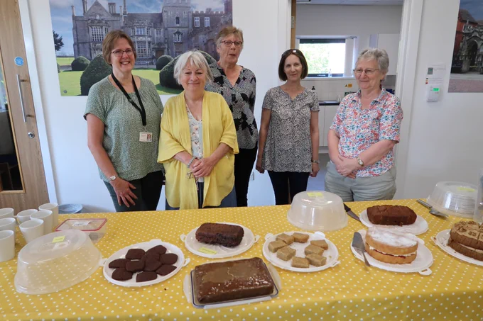  5 people and a table full of cakes on a yellow spotted table cloth.