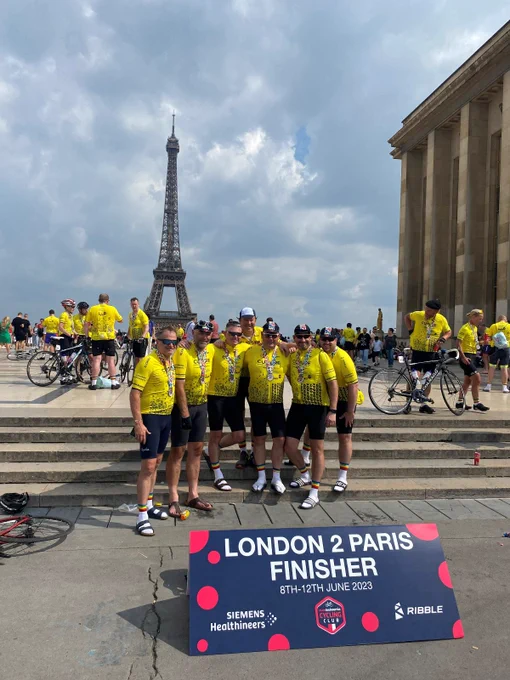 Seven males stood in front of the Eiffel Tower wearing medals