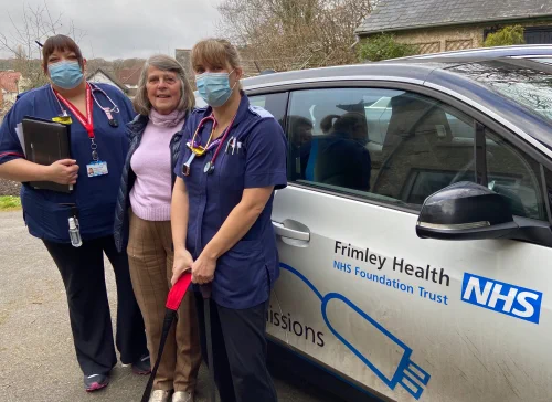 Three clinicians stand outside a car that reads 'Frimley Health, NHS Foundation Trust' 