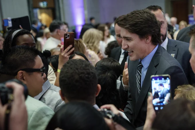 Prime Minister Justin Trudeau is standing in a crowd of people and speaking with a man. Both of them are smiling.