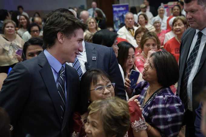 Prime Minister Justin Trudeau is standing in a crowd of people and speaking with a woman. Both of them are smiling.