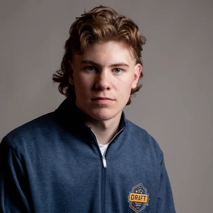 Oliver Bonk posing for a photo in a blue NHL Draft quarter-zip. He's sporting a medium-length mullet. 